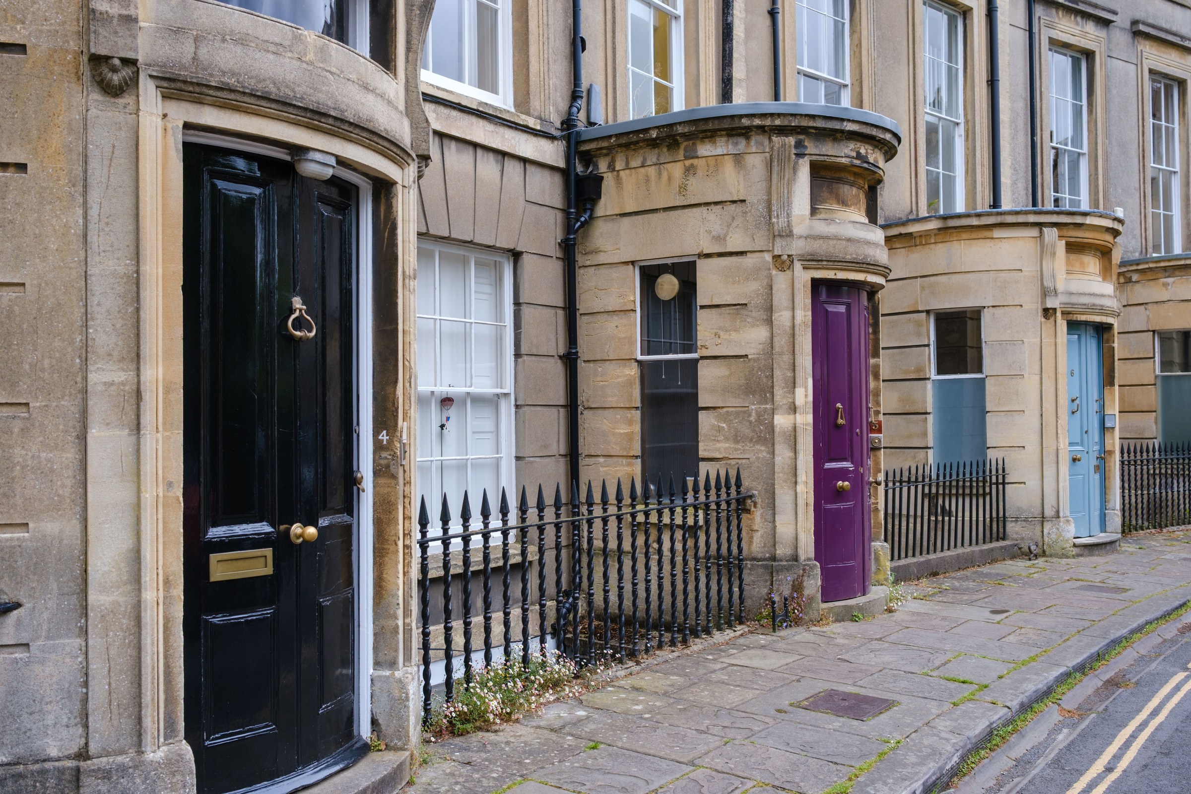 Georgian Bath-stone terrace: a glossy black door on the left, then a purple door and a blue door further along the street